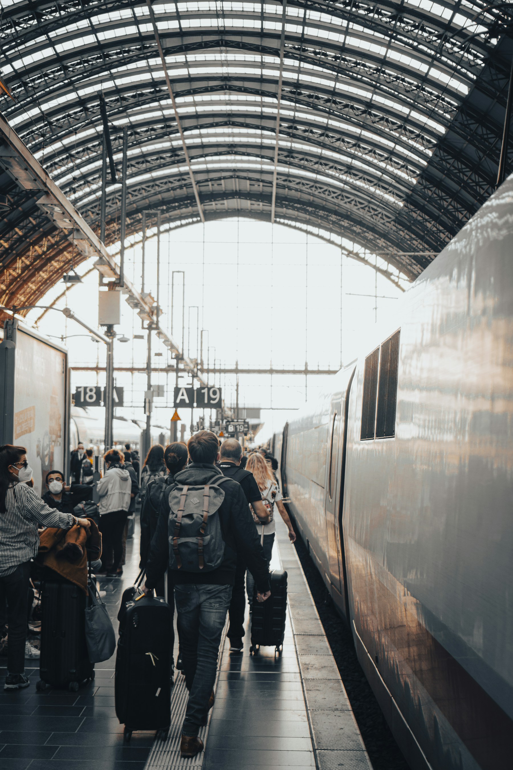 Reisende mit Rollkoffern am Bahnsteig neben einem Zug