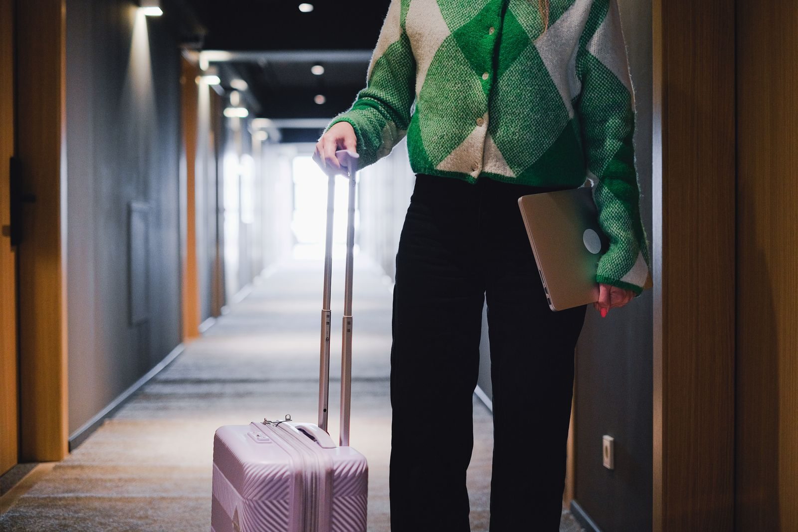 Person mit Laptop und Rollkoffer im Hotelkorridor